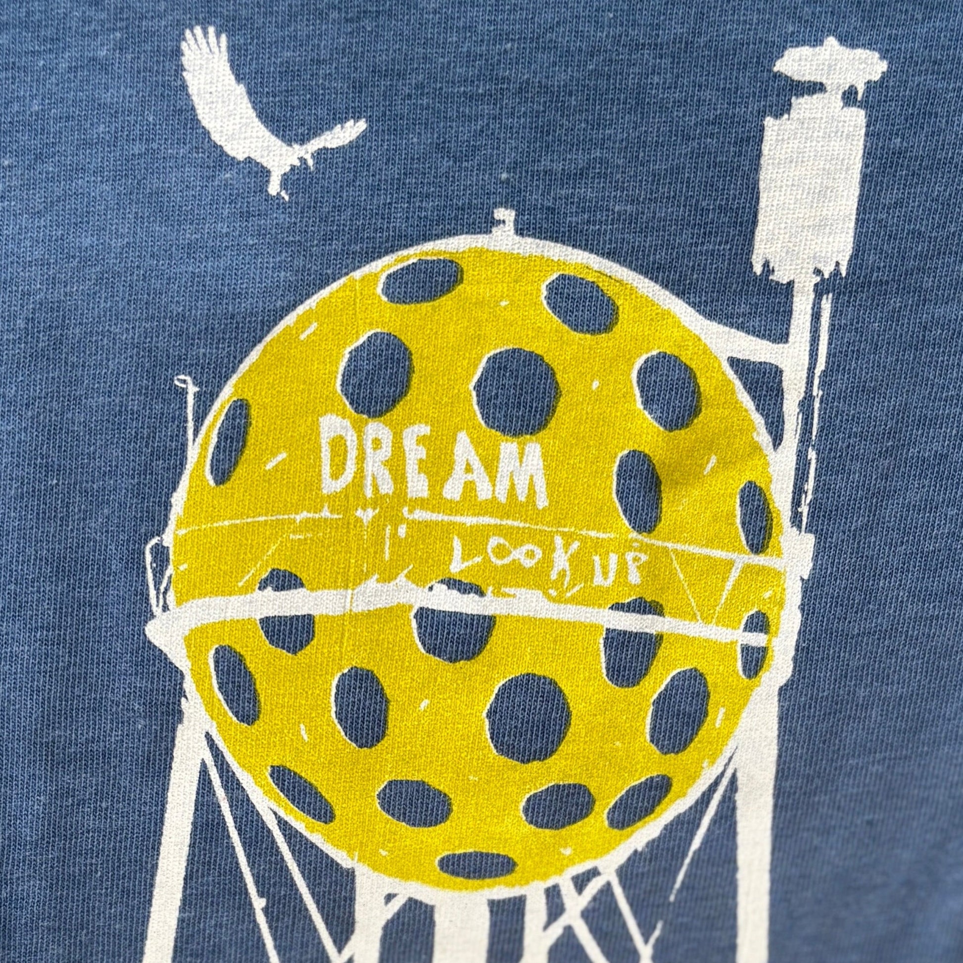 Sea blue t-shirt with a graphic of a water tower and pickleball, featuring text on a blue background.