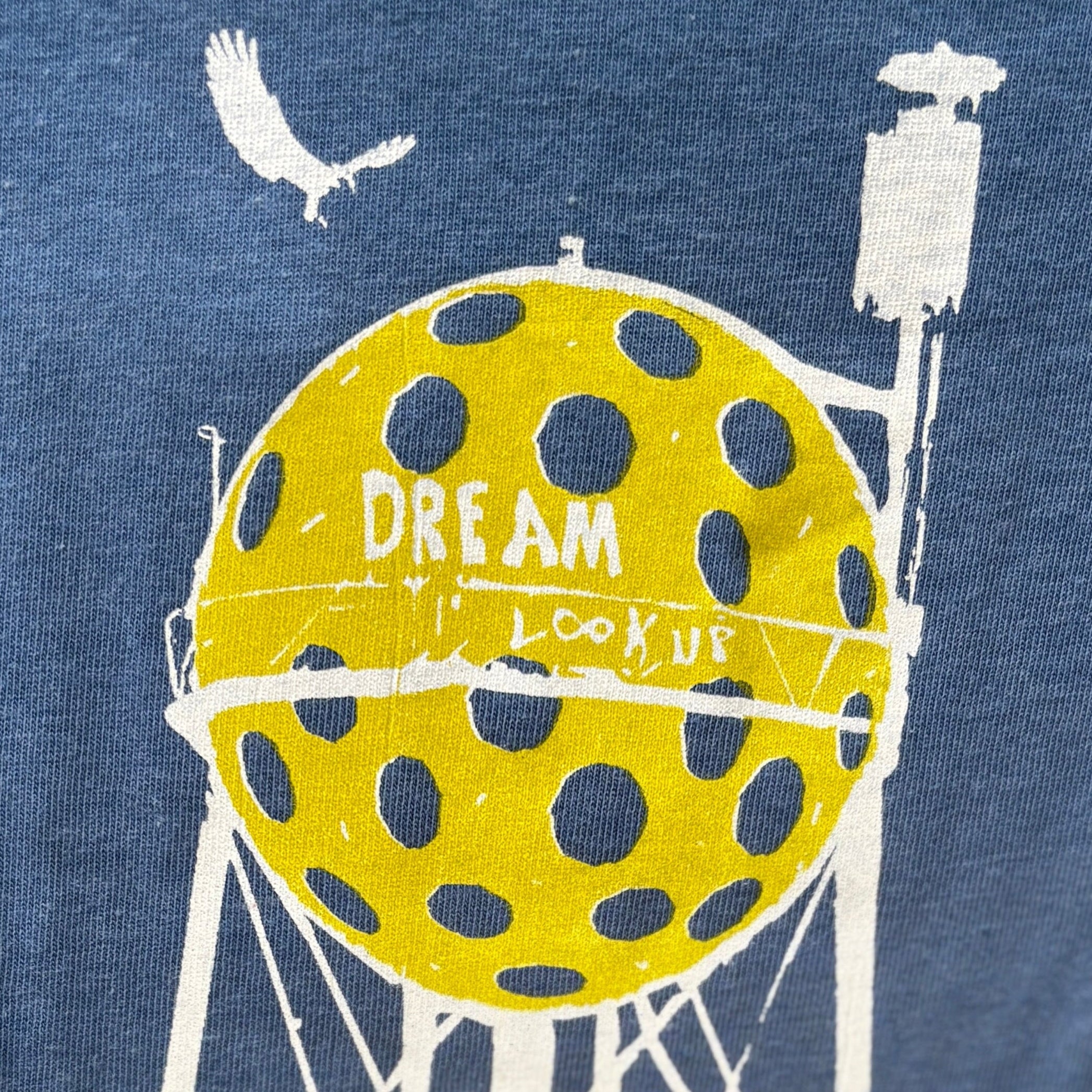 Sea blue t-shirt with a graphic of a water tower and pickleball, featuring text on a blue background.