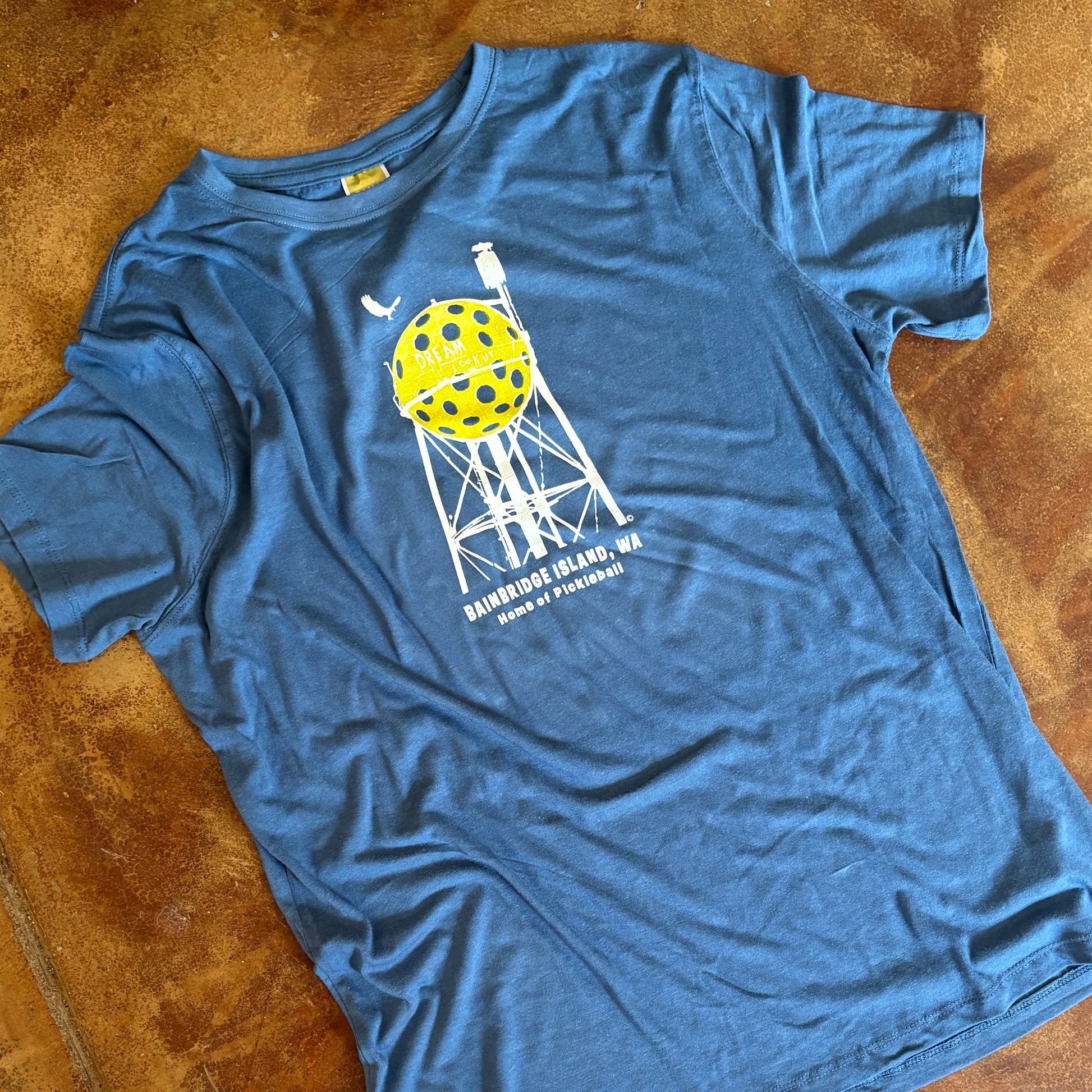 Blue t-shirt with a pickleball tower graphic design on a concrete floor